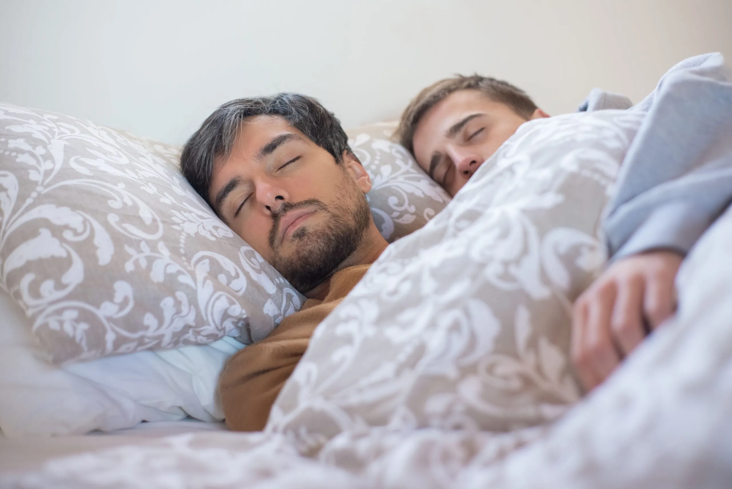 A loving couple peacefully sleeping together, embracing under a warm blanket indoors.