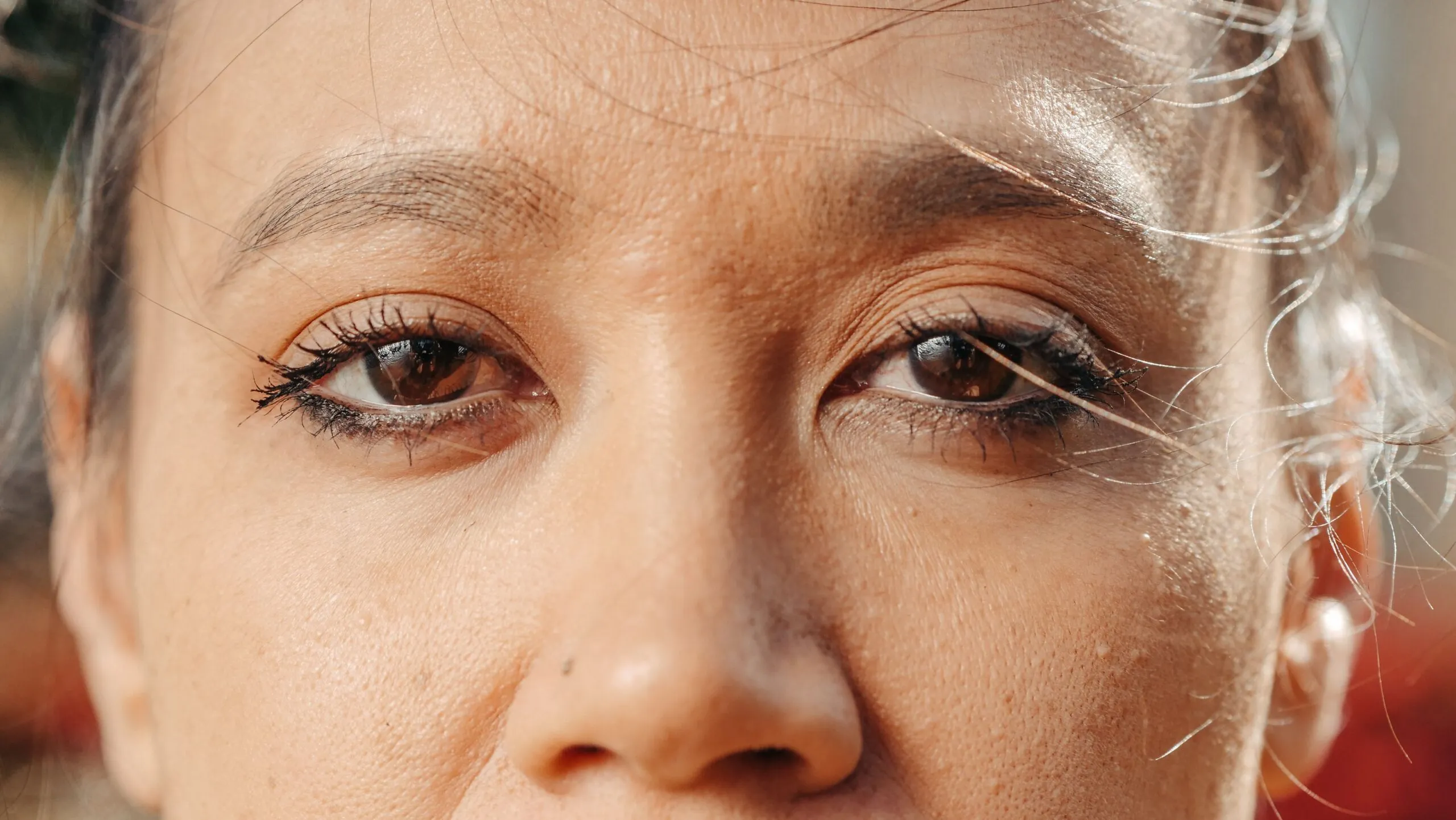 Extreme close-up of a woman's eyes with soft natural lighting, showcasing eye makeup and skin texture.