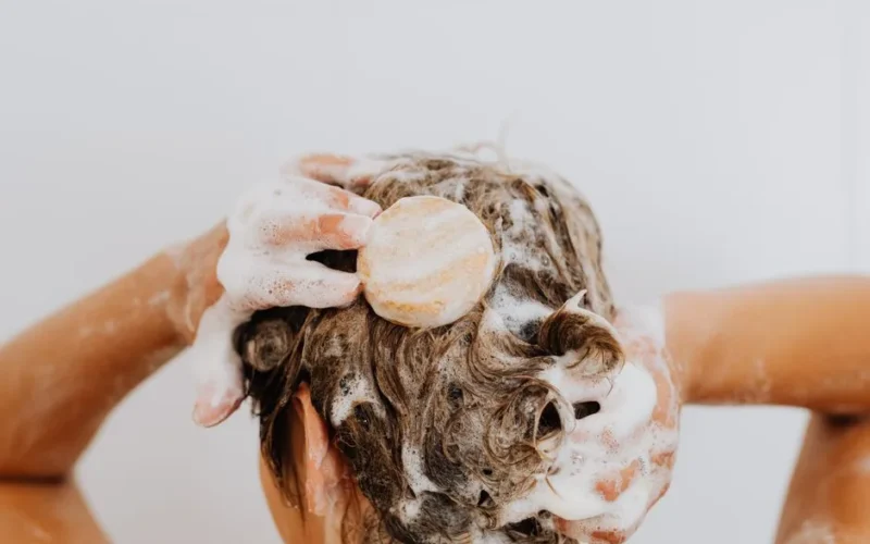 Close-up of a person washing their hair with soap bar and foam, focusing on hands and hair.