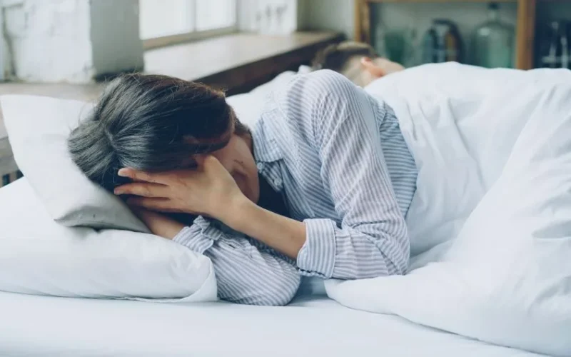 A woman in bed showing signs of anxiety. Soft light indoors.