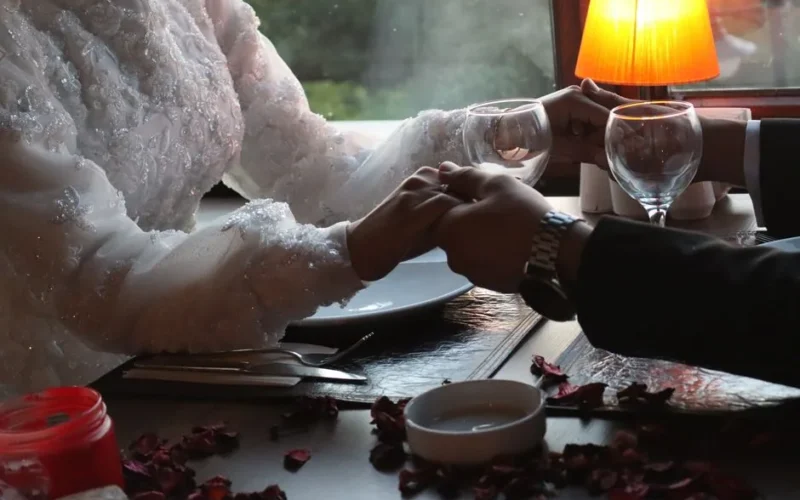Bride and groom holding hands at a romantic dinner setting with soft lighting.