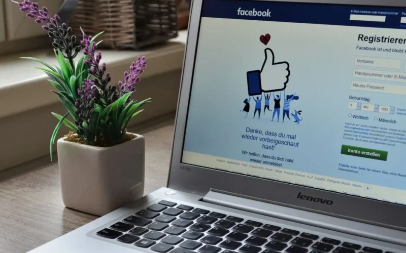 A Lenovo laptop displaying Facebook login beside a lavender plant indoors.