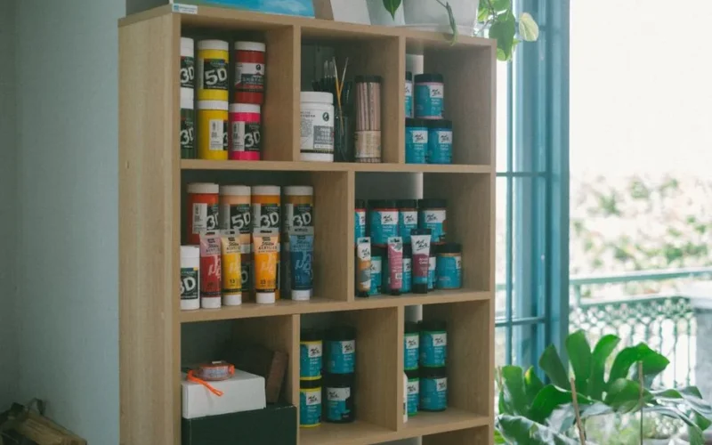 Wooden shelf filled with colorful art supplies in a bright, airy studio.