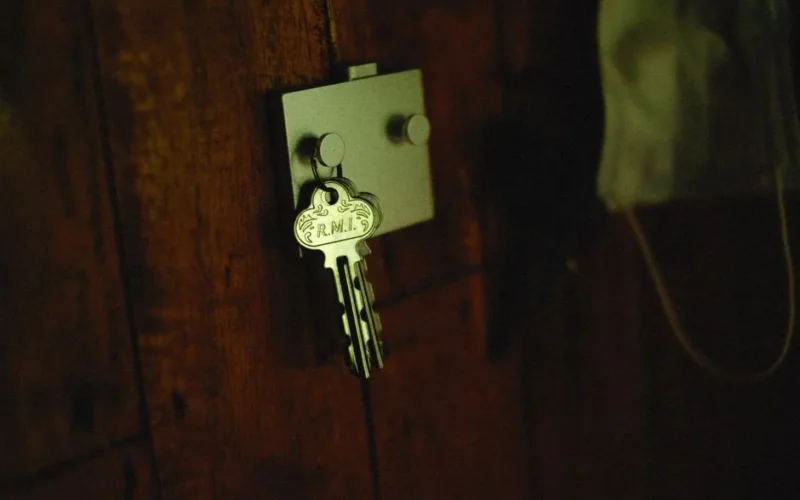 A close-up of a metallic key labeled 'R.M.I.' on a rustic wooden wall hook.