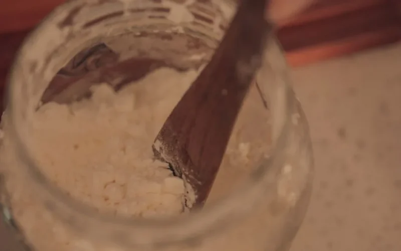 Close-up of wooden spoon stirring powdered ingredient in a glass jar.