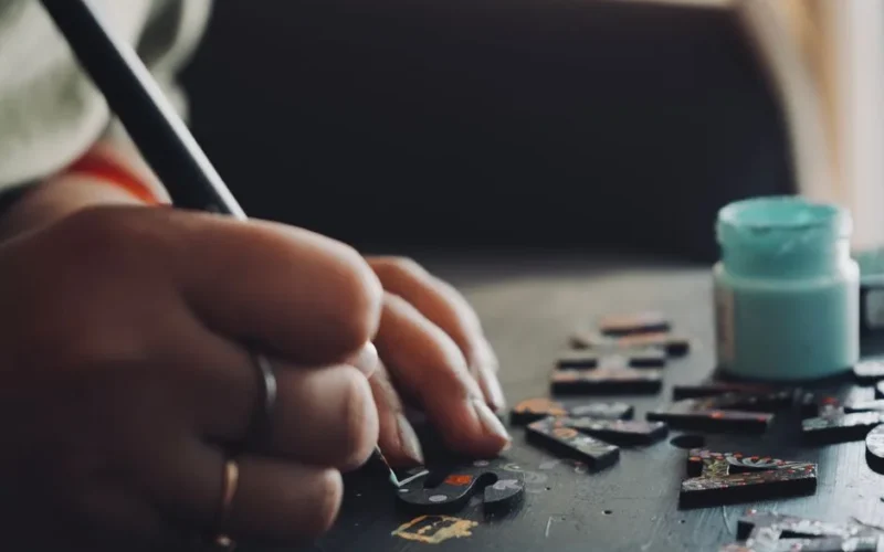 Detailed view of a hand using a brush to paint puzzle pieces, showcasing artistic creativity and precision.