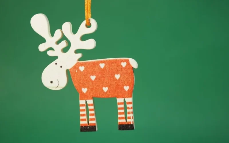 A charming reindeer ornament with heart patterns hanging against a green backdrop, perfect for Christmas decor.