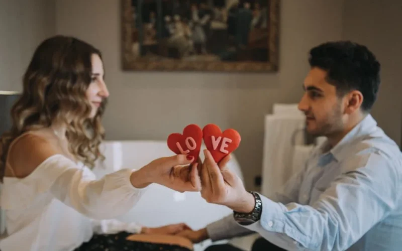 A couple sharing a romantic moment indoors, holding heart-shaped love symbols, enhancing a Valentine's Day feel.