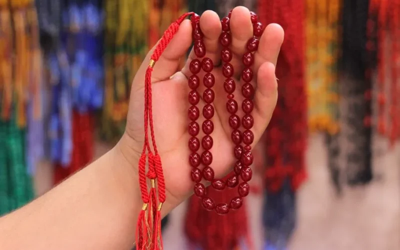 A close-up view of red prayer beads held in a hand, with colorful background in Adana, Türkiye.