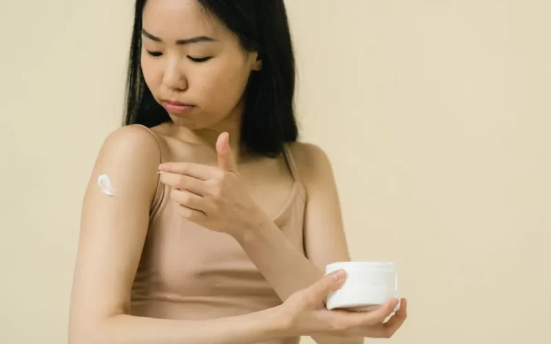 A woman applies moisturizing cream on her arm, focusing on skincare and self-care.