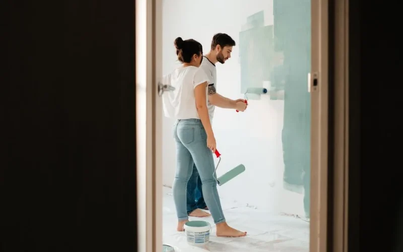 A man and woman painting a room wall with rollers, showcasing teamwork in home renovation projects.