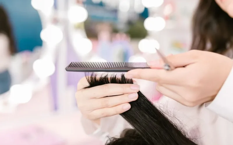Close-up of a hairdresser grooming hair with scissors and a comb in a salon setting.
