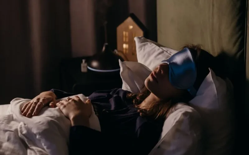 A woman resting with a sleep mask in a calm bedroom setting, creating a serene and cozy atmosphere.