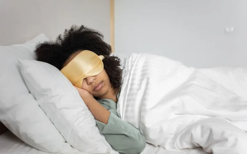 A woman peacefully sleeping with an eye mask in a cozy white bedroom setting.