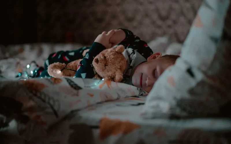 A young child peacefully sleeping in bed, hugging a teddy bear close, creating a cozy bedtime atmosphere.