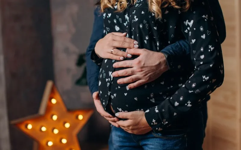 A couple lovingly embraces a pregnant belly indoors, with a star-shaped light in the background.
