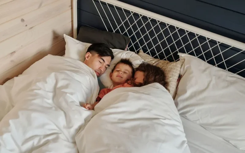 A family peacefully sleeping together in a cozy bedroom setting, showcasing warmth and togetherness.