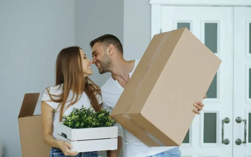 Happy couple carrying boxes and plants, beginning life in a new home.