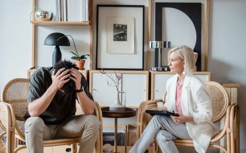 Professional therapy session with a stressed man and attentive female therapist in a modern office setting.