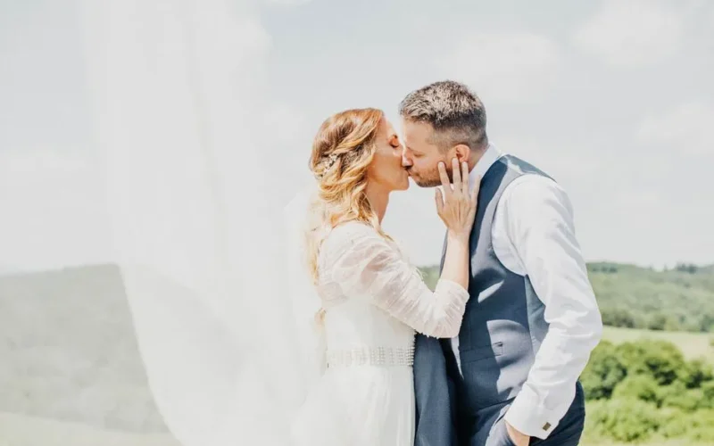 A bride and groom share a romantic kiss amidst a scenic outdoor backdrop, celebrating their love.