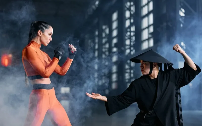 Two cosplayers engage in a dynamic martial arts duel amidst dramatic fog, indoors.