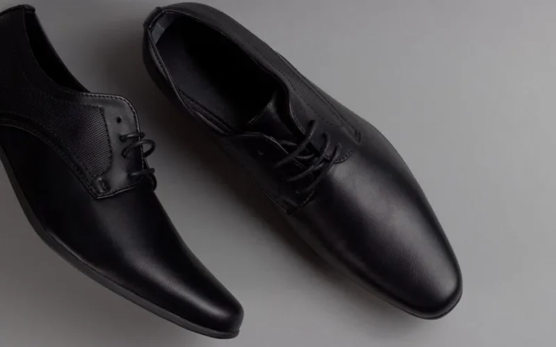 Pair of stylish black formal shoes displayed on a minimalist grey background, perfect for business attire.