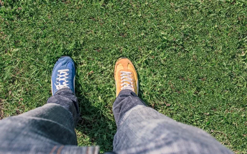 A person wearing mismatched shoes stands on green grass, highlighting differences and individuality.