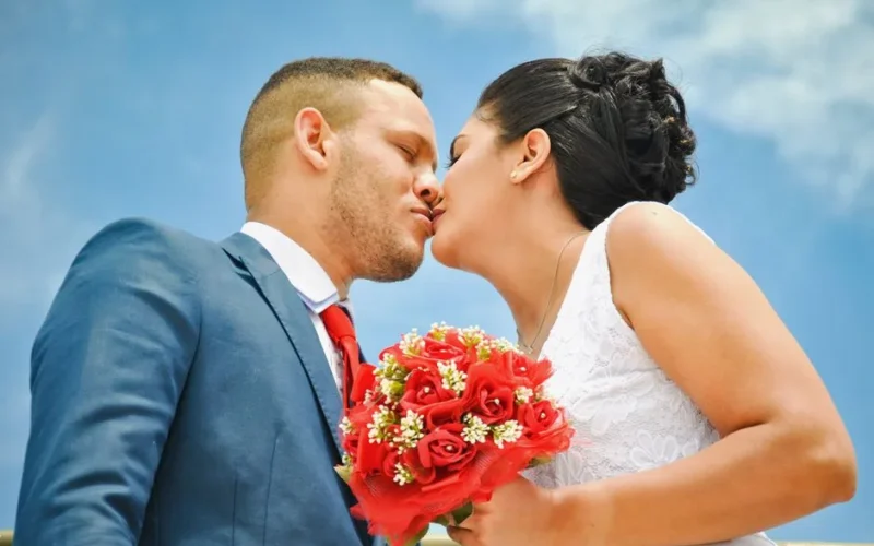 A romantic moment between a bride and groom kissing passionately outdoors with a beautiful bouquet.