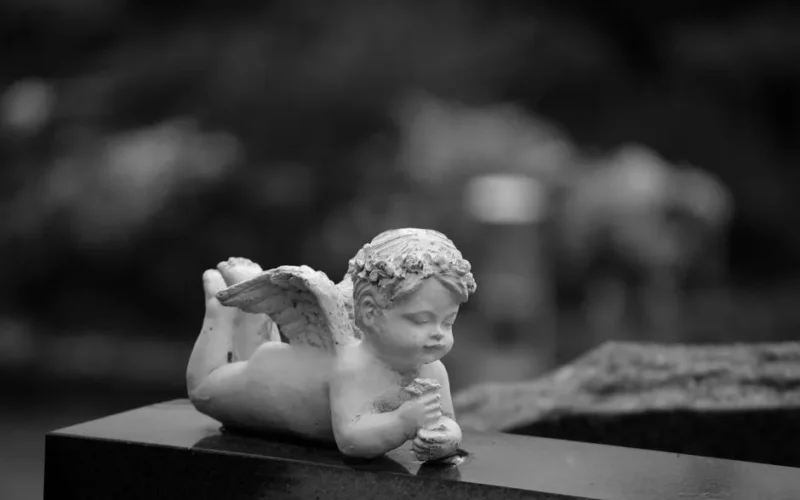 Black and white image of an angel statue at a cemetery symbolizes peace and remembrance.