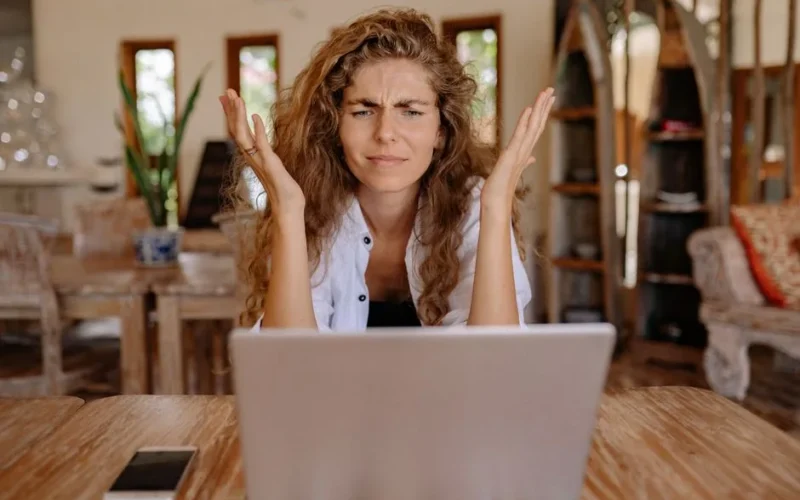 A woman frustrated with her laptop while working remotely indoors, expressing stress.