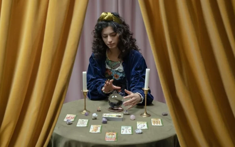 A woman performs fortune telling with a crystal ball and tarot cards, creating a mystical atmosphere.