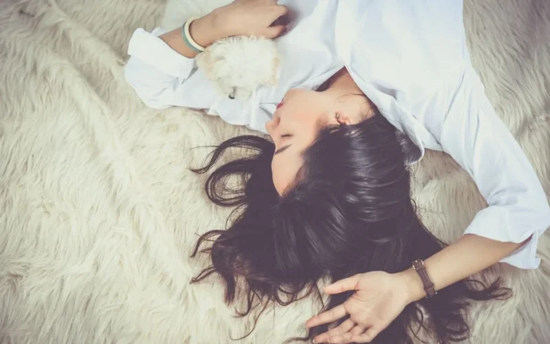 A woman peacefully sleeping with her pet dog on a soft, furry rug indoors.