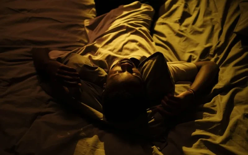 A man lies in bed at night, struggling with insomnia in a dimly lit room.