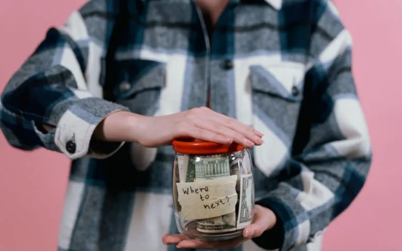 Woman in plaid shirt holds money jar with travel goals in mind.