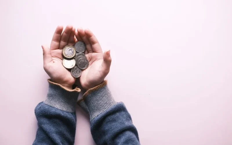 Close-up of hands in sweater holding various coins, indicating savings and finance on a white background.