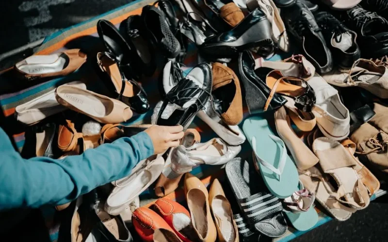 A variety of footwear displayed at an outdoor market stall with a hand selecting a shoe.