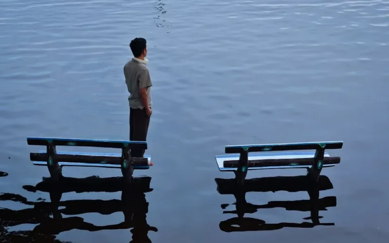 A man stands between benches in a flooded area, creating a contemplative scene.