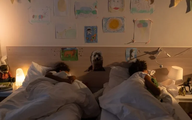 Two children asleep in a cozy bedroom with wall drawings, soft lighting, and comforting decor.