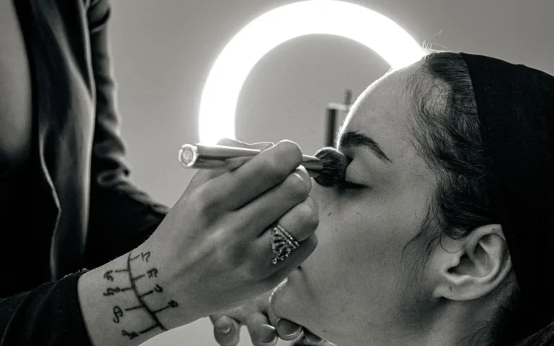 A makeup artist applies professional makeup to a woman with a brush in a studio setting.