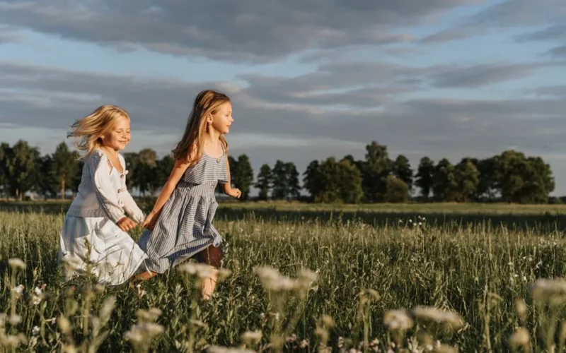 Two girls running happily in a sunny field, enjoying a carefree day outdoors.