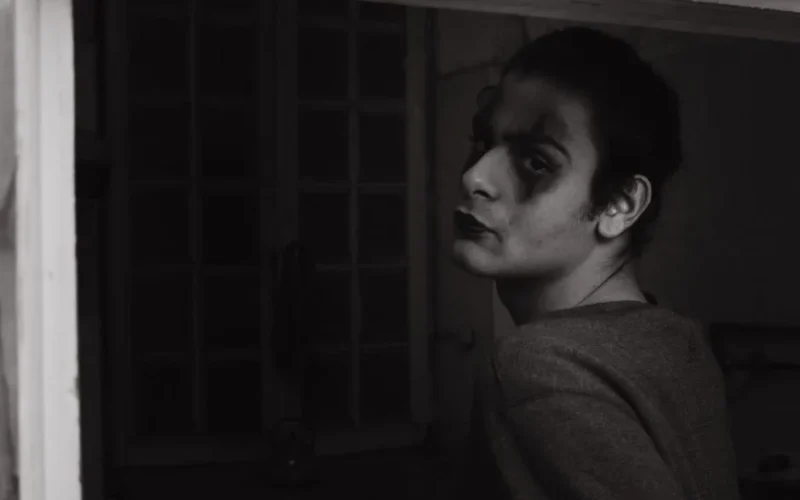 Eerie black and white portrait of a person with Joker makeup looking over their shoulder.