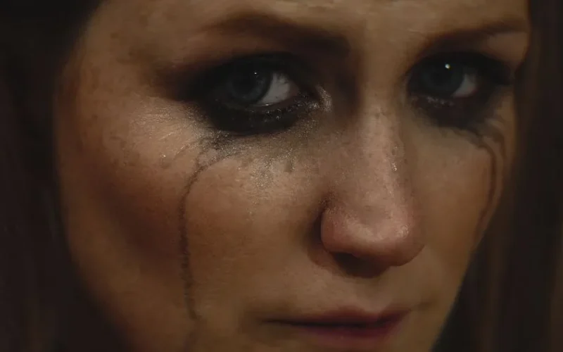 Close-up of a woman with smeared makeup and tears on her face showing deep emotion.