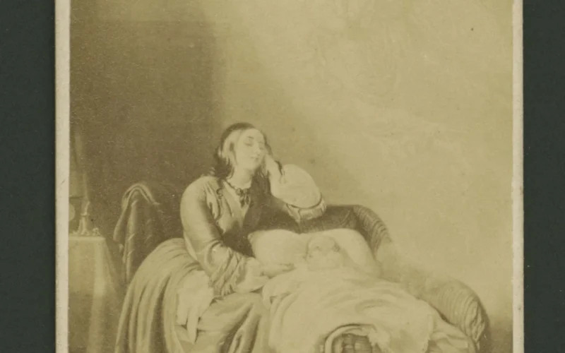 Printed card bearing an image of a woman dozing beside her infant as an angel hovers in a shaft of light above her. The angel is holding a baby in her arms. Titled "The Mother's Dream."