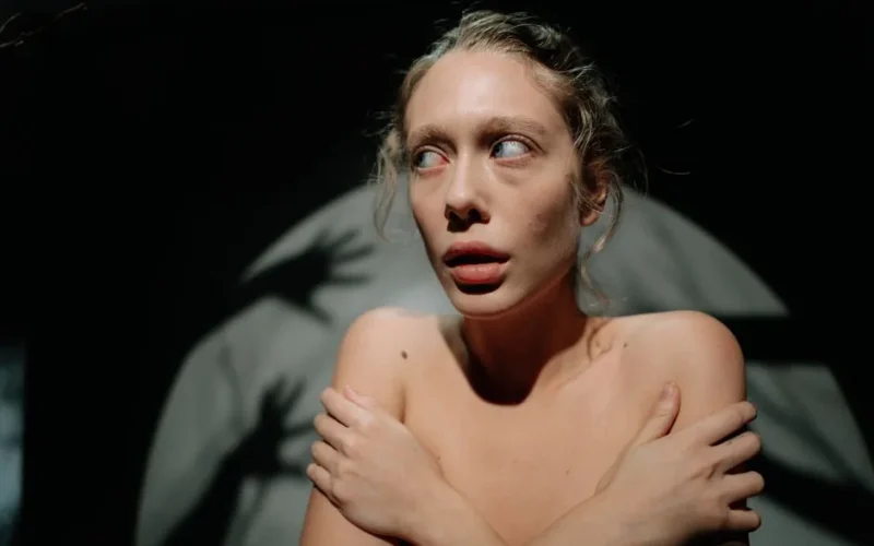 A woman in dramatic lighting, surrounded by shadows, looking anxious.
