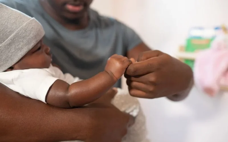 Heartwarming scene of a father gently holding his infant's hand indoors.