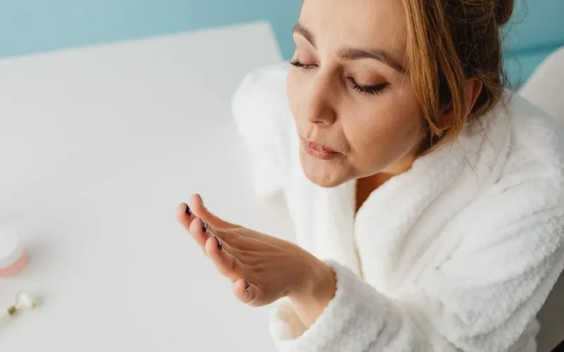 Woman in a bathrobe blowing on freshly painted nails, focusing on self-care and relaxation indoors.