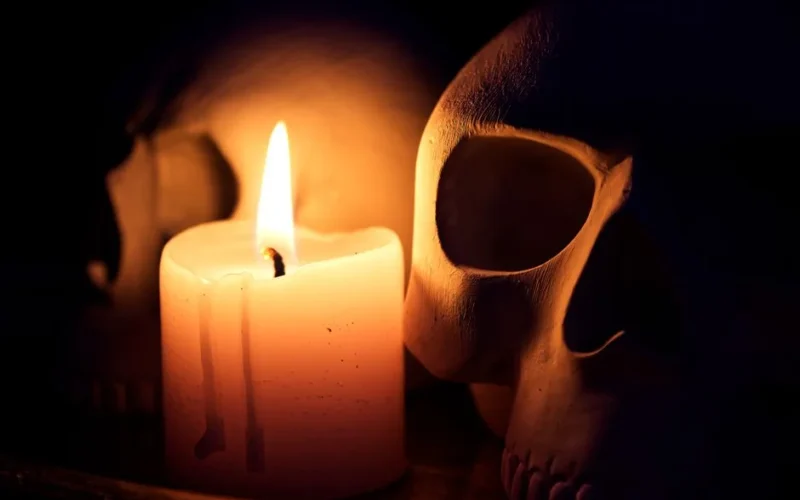 A dramatic still life featuring a candle illuminating two human skulls in the dark.