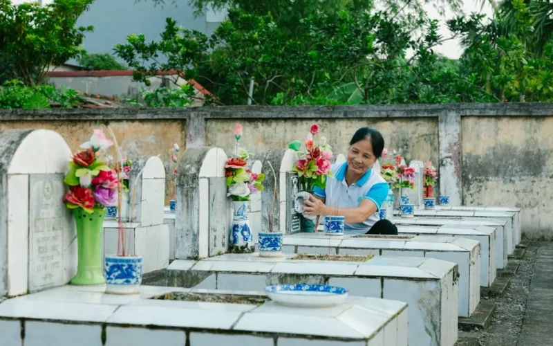 A woman cleans gravestones and places colorful flowers in a peaceful cemetery setting.