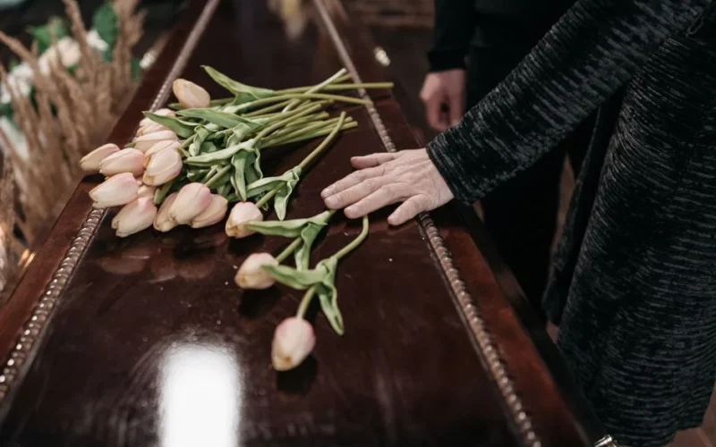 A somber funeral scene with tulips placed on a wooden coffin, symbolizing loss and remembrance.