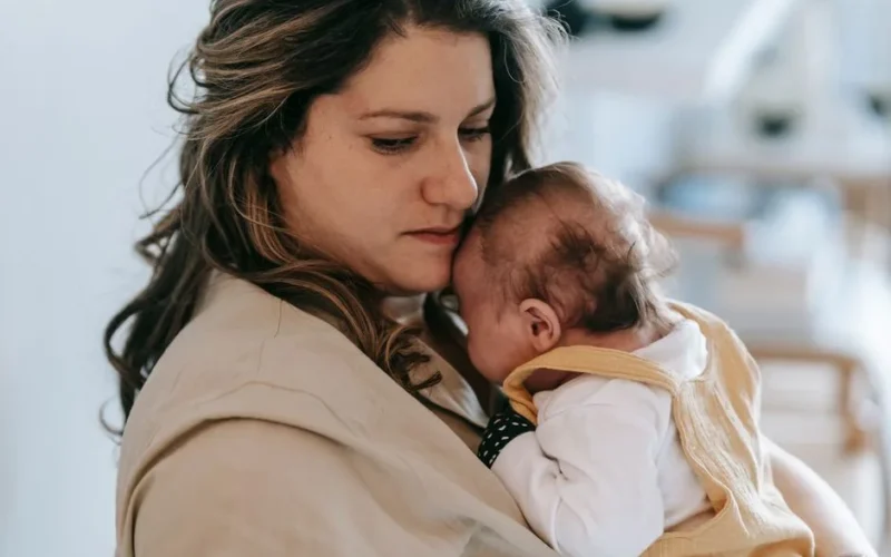 A mother gently holding her baby in a comforting embrace inside a cozy home setting.